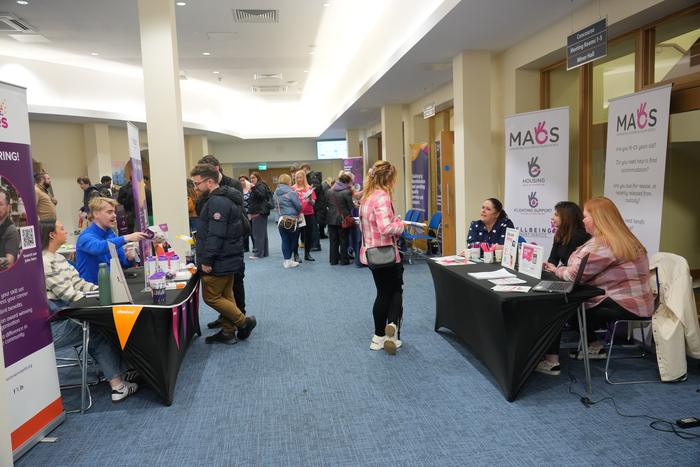 Visitors browsing charity stands along a wide carpeted aisle at the job fair