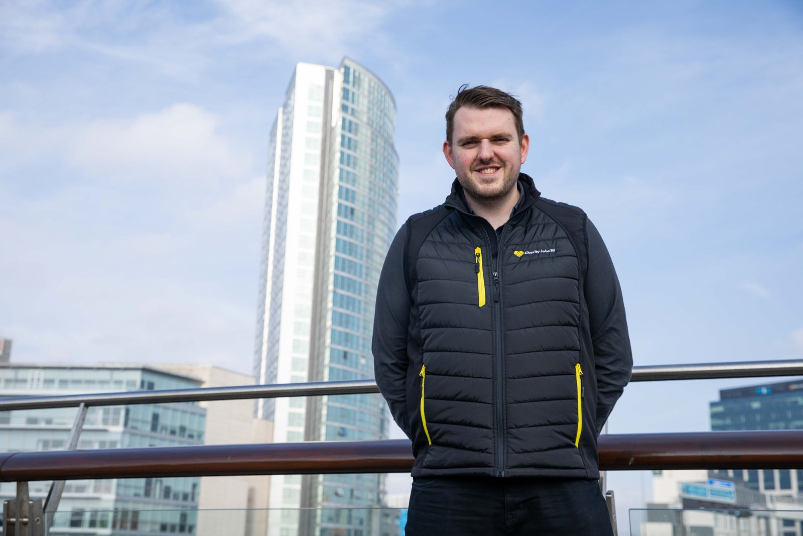 A Charity Jobs NI representative standing outdoors in Belfast with a high-rise building behind him