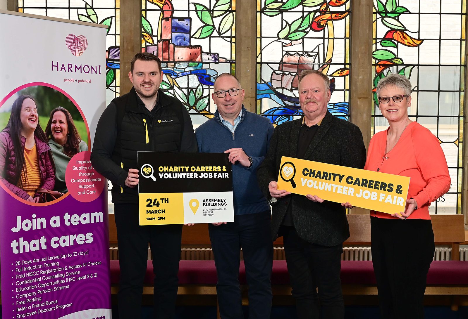 Four people holding Charity Careers & Volunteer Job Fair boards beside a Harmoni recruitment banner