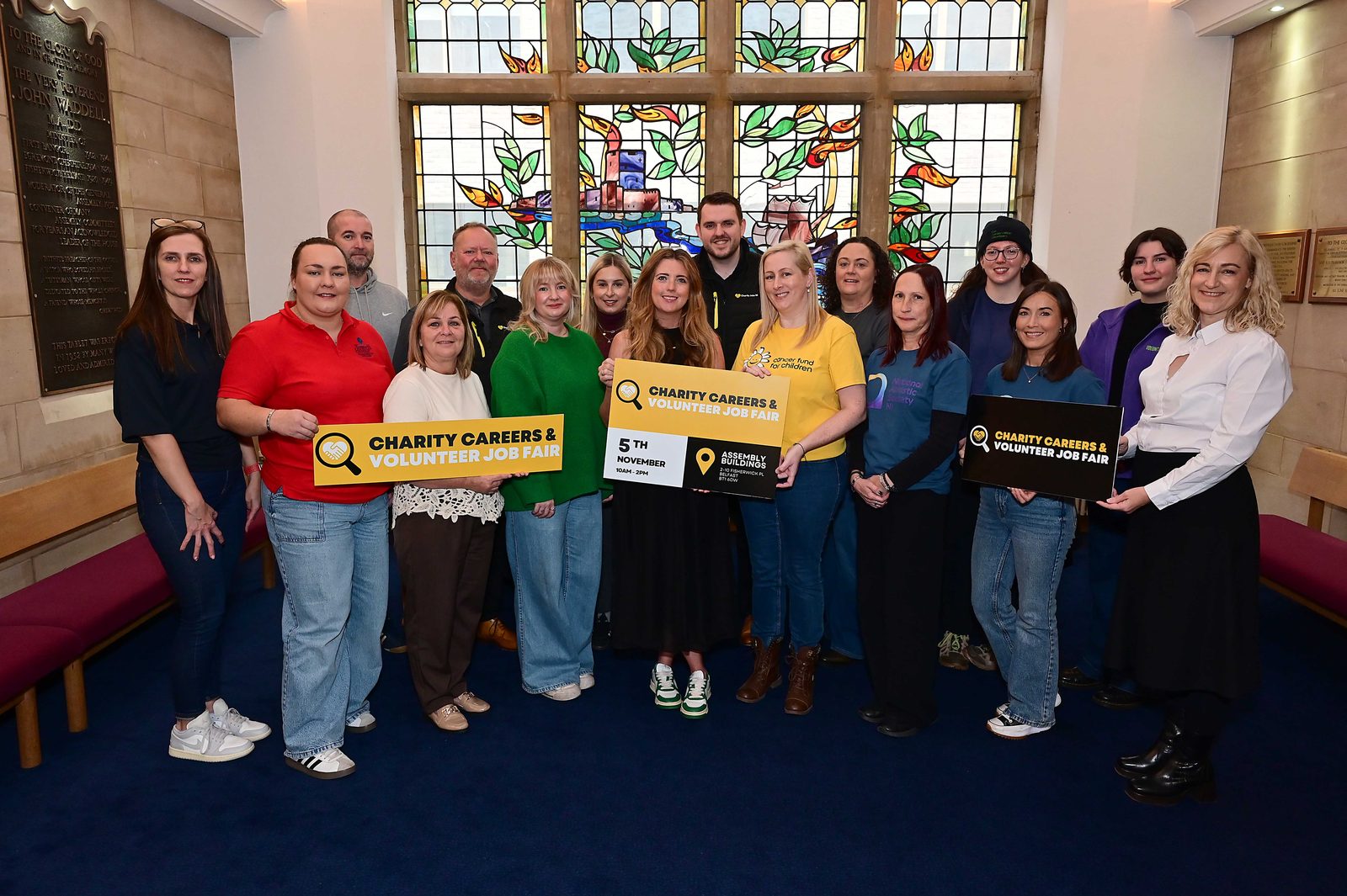 A large group of charity staff holding job fair boards in the hall at Assembly Buildings, Belfast