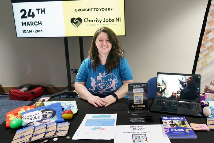 A charity exhibitor seated at a fully branded stand with fair signage behind