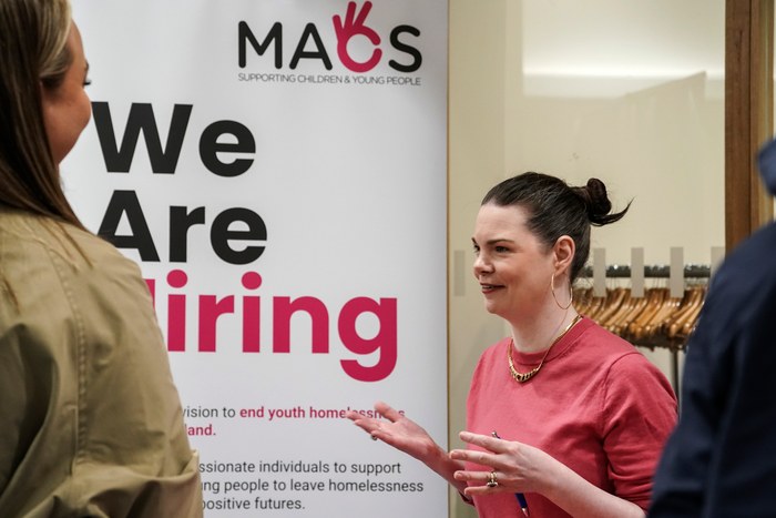 A charity representative talking to a visitor beside a We Are Hiring banner