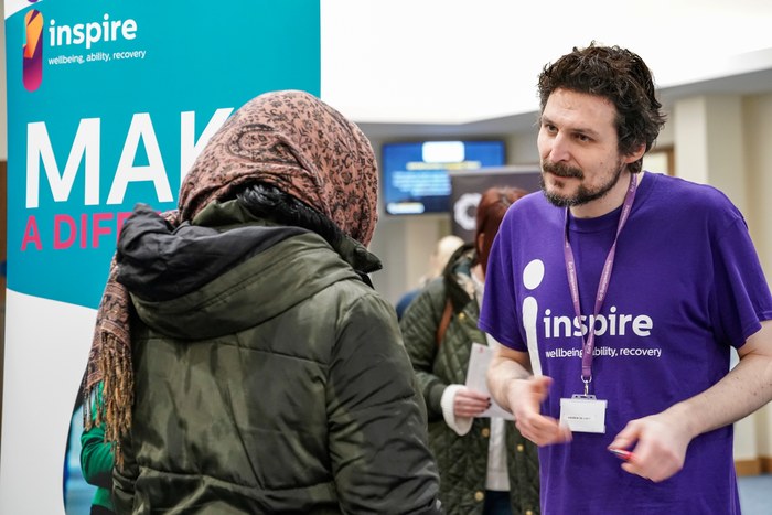 An Inspire staff member in a purple t-shirt talking with a visitor