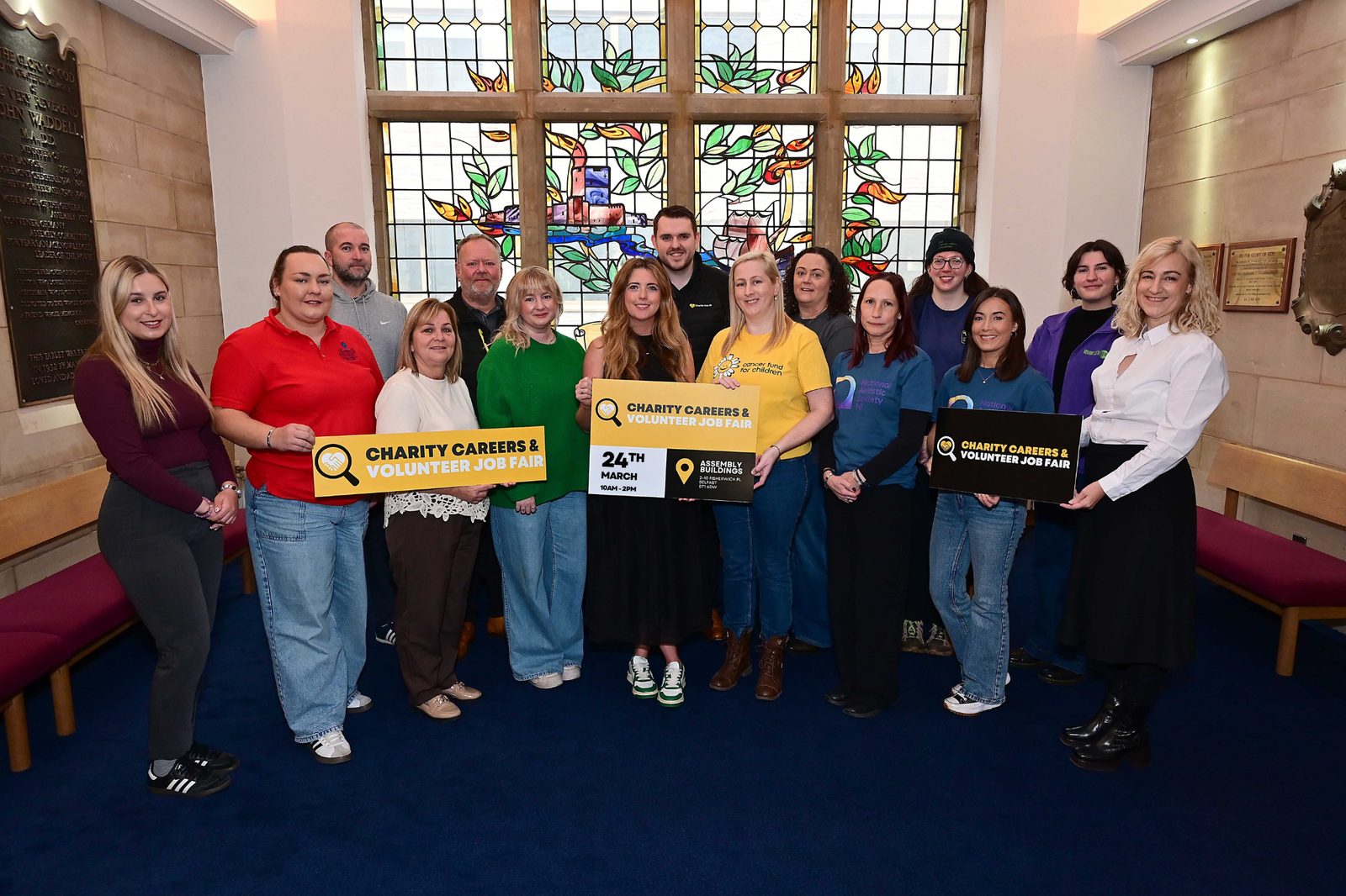 A large group of charity representatives holding Charity Careers & Volunteer Job Fair boards inside Assembly Buildings, Belfast
