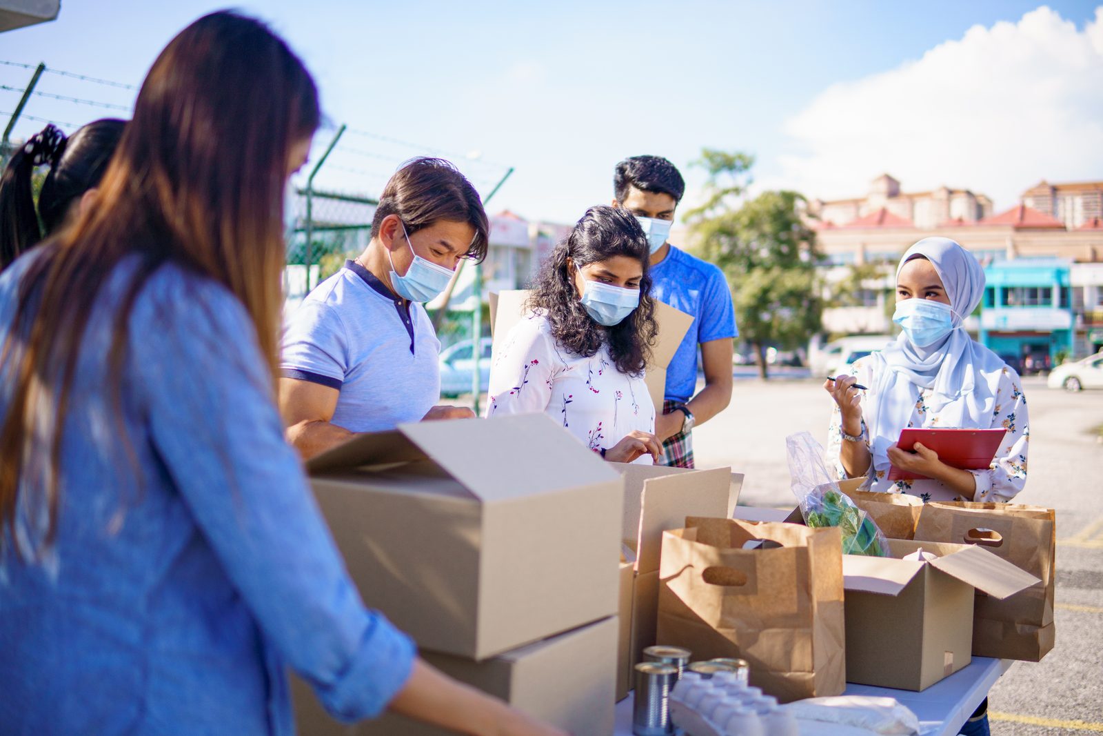 Volunteers in aprons and face coverings packing cardboard boxes of food outdoors