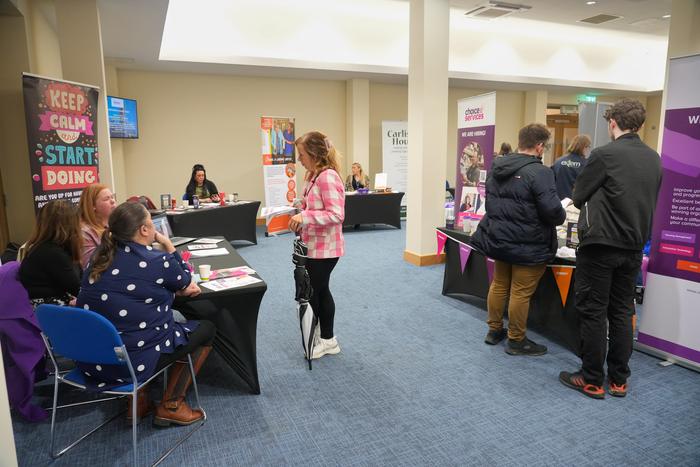 A busy exhibition hall at the Charity Careers and Volunteer Job Fair, with rows of charity stands and visitors talking to staff